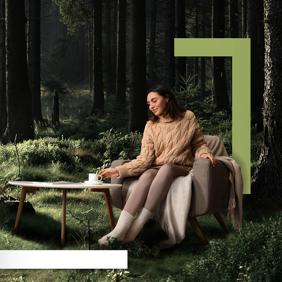 Bilde av dame i skogen som sitter på sofa og drikker kaffe, for Romsly - Grønne modulhus